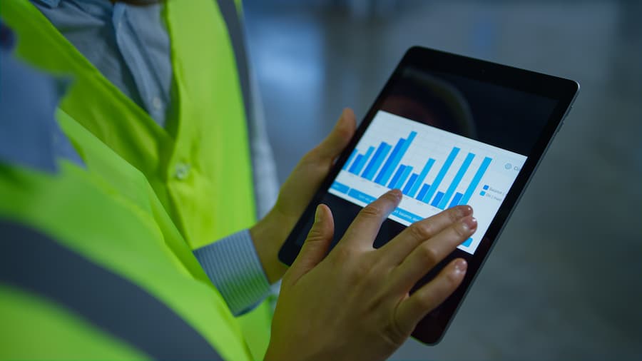 An Ipad showing warhouse statistics held by two workers wearing safty vests